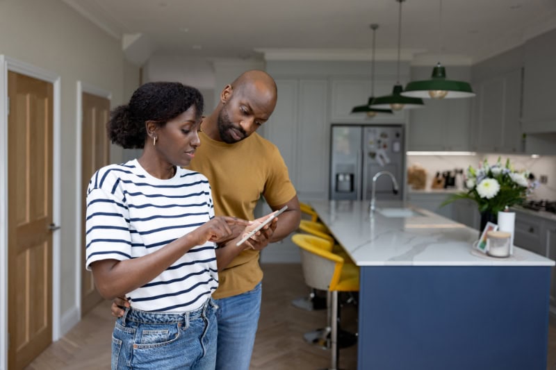 Husband and wife standing in kitchen looking over bill.